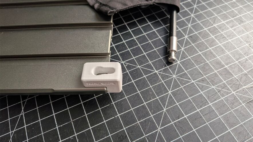 Close-up of a gray metal toolbox accessory with a small white plastic end cap on a grid-cutting mat.