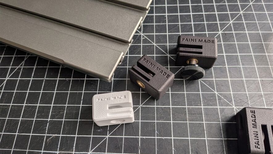 Assorted small plastic clamps on a dark grid cutting mat, with a stack of gray metal pieces to the left.