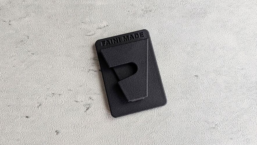 Black rectangular tag with 'FAN MADE' embossed on a gray textured surface.