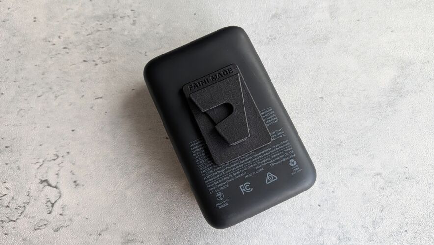 Back of a black rectangular charger with a fold-out clip on a light gray textured surface.